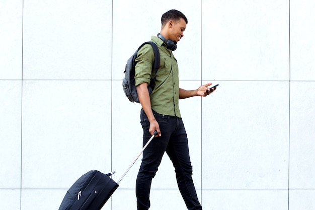 Junger reisender Mann, der mit Koffer und Mobiltelefon geht