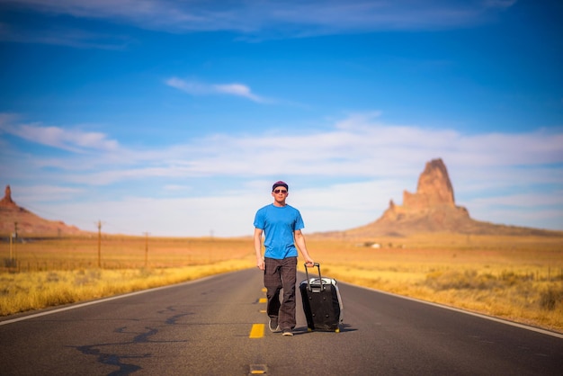 Junger reisender mit einem koffer, der auf einer straße in arizona geht