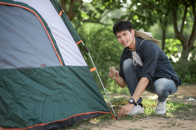 Junger Reisender verwendet einen Stein, um beim Campingausflug im Sommerurlaub auf die Zeltheringe im Wald zu schlagen