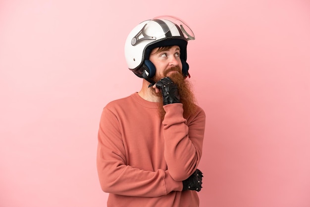 Junger rötlich-kaukasischer Mann mit einem Motorradhelm auf rosa Hintergrund isoliert und nach oben schauend