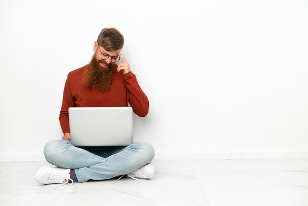 Junger rötlich kaukasischer Mann mit Laptop auf weißem Hintergrund lachend