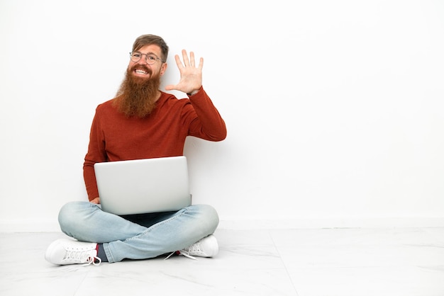 Junger rötlicher kaukasischer Mann mit Laptop lokalisiert auf weißem Hintergrund, der fünf mit den Fingern zählt