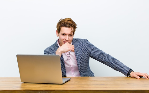 Junger roter Hauptgeschäftsmann, der in seinem Schreibtisch mit einem Laptop arbeitet