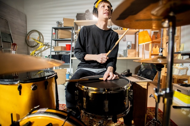 Junger Schlagzeuger mit Kopfhörern schlägt Becken und Trommel mit Trommelstöcken während der Einzelprobe und der Aufnahme seiner Musik