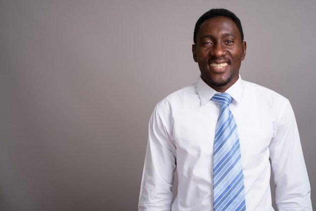 Junger schöner afrikanischer Geschäftsmann gegen grauen Hintergrund