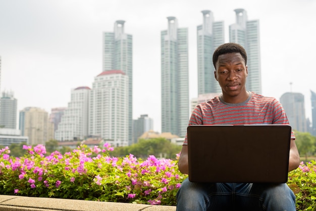 Junger schöner afrikanischer Mann, der Laptop-Computer im Park verwendet