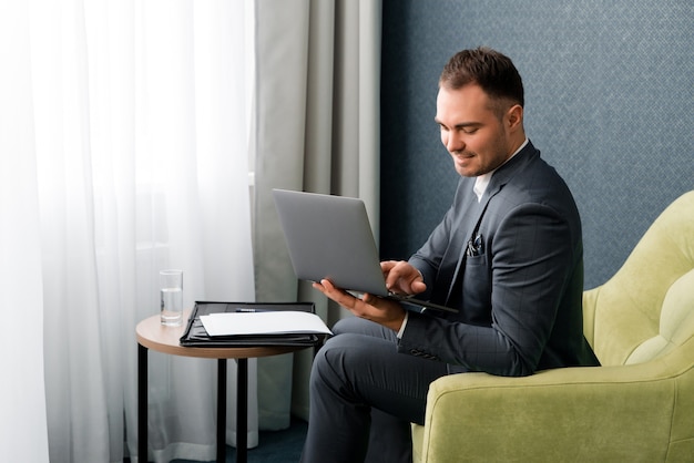 Junger schöner Geschäftsmann, der mit Laptop im Hotelzimmer arbeitet