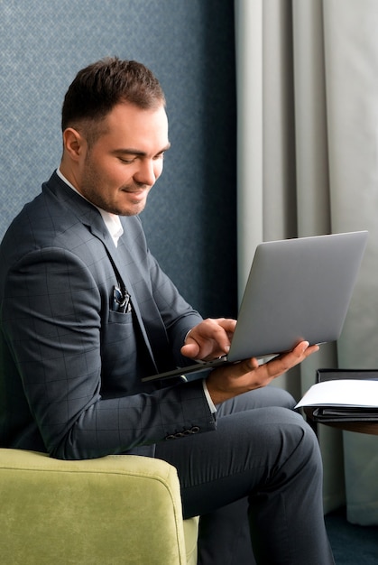 Junger schöner Geschäftsmann, der mit Laptop im Hotelzimmer arbeitet