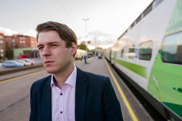 Junger schöner Geschäftsmann, der vor Zug am Bahnhof denkt