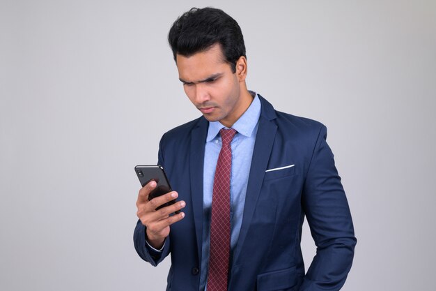 Junger schöner indischer Geschäftsmann, der Anzug auf Weiß trägt