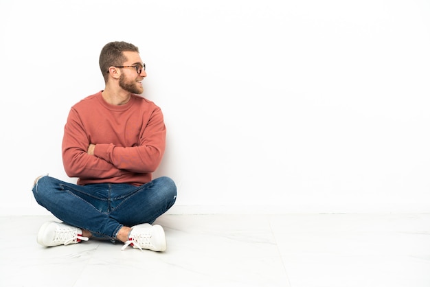 Junger schöner Mann, der auf dem Boden in der seitlichen Position sitzt