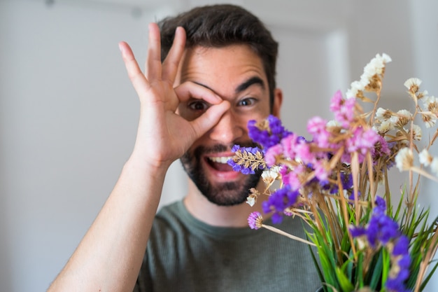 Junger schöner Mann, der Blumen zu Hause hält