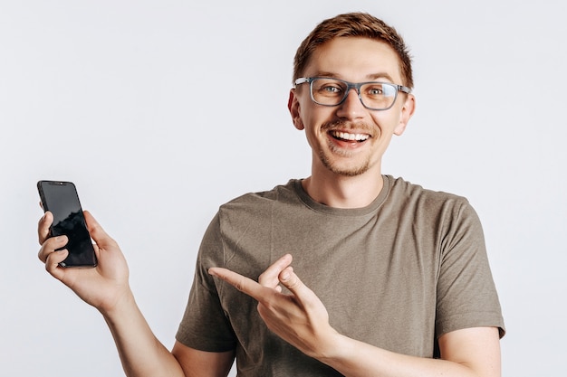 Junger schöner Mann, der ein Smartphone hält und auf grauem isoliertem Raum lächelt