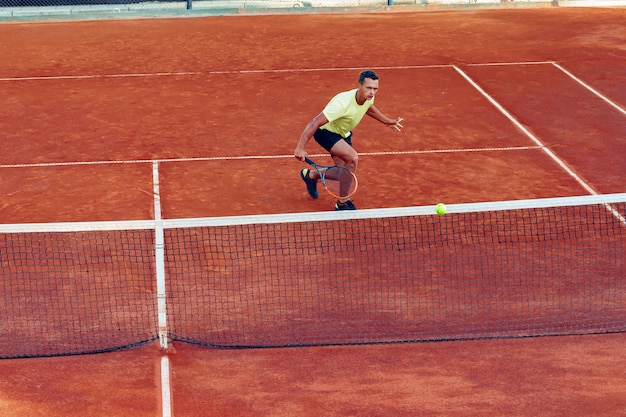 Junger schöner Mann, der Tennis auf dem Tennisplatz spielt