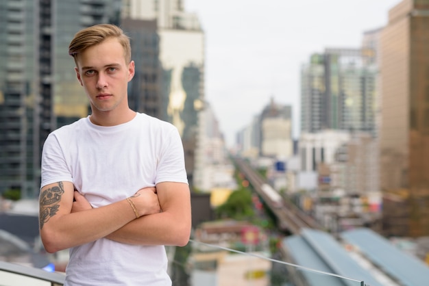 Junger schöner Mann mit blondem Haar gegen Ansicht der Stadt