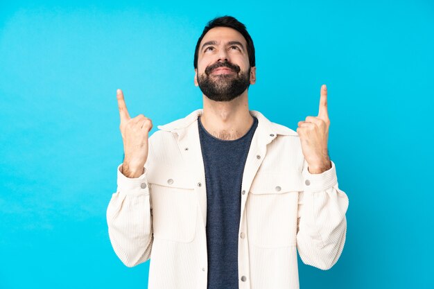 Junger schöner Mann mit weißer Cordjacke über isolierter blauer Wand, die eine große Idee aufzeigt