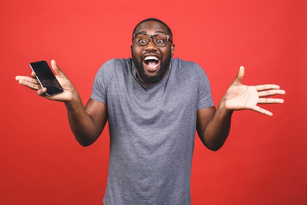Junger Schwarzafrikaner, der leeres Smartphone hält, Bildschirm zeigt, sich glücklich und überrascht fühlt