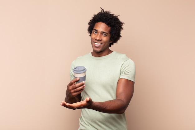 Junger schwarzer Afro-Mann, der fröhlich lächelt, sich glücklich fühlt und ein Konzept im Kopienraum mit Handfläche zeigt