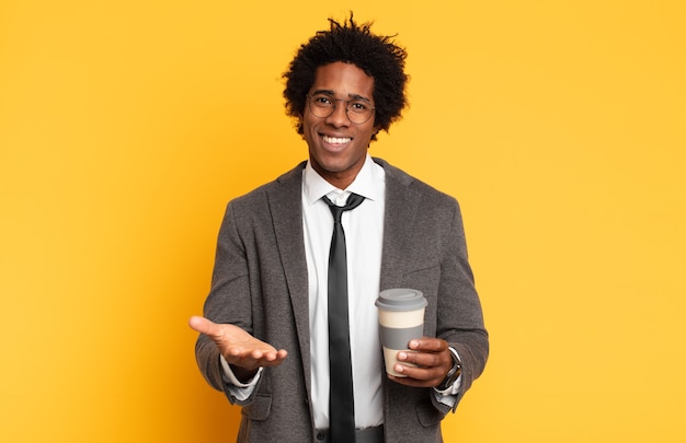 Junger schwarzer Afro-Mann, der glücklich mit freundlichem, selbstbewusstem, positivem Blick lächelt und ein Objekt oder Konzept anbietet und zeigt