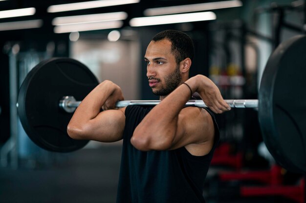 Junger schwarzer männlicher Athlet, der mit schwerer Langhantel im Fitnessstudio trainiert