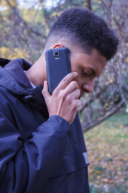 Junger schwarzer Mann, der am intelligenten Telefon im Wald spricht.