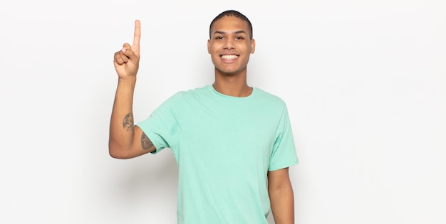 Junger schwarzer Mann, der fröhlich und glücklich lächelt und mit einer Hand nach oben zeigt, um den Raum zu kopieren