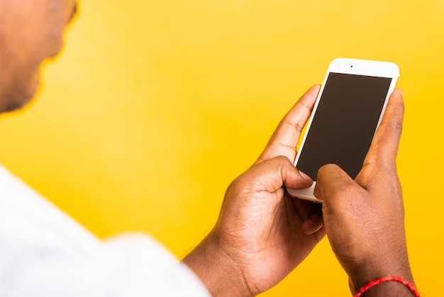 Junger schwarzer Mann des asiatischen glücklichen Porträts der Nahaufnahme, der leeren Bildschirmraum des digitalen mobilen Smartphones auf Händen hält, Studio lokalisiert auf gelbem Hintergrund