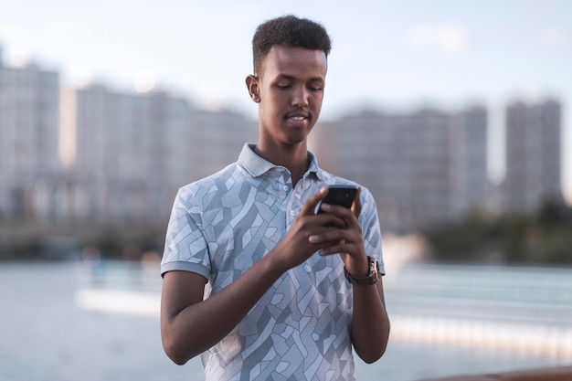 Junger schwarzer mann in lässiger kleidung, der eine sms mit seinem handykopienraum tippt, umfasst