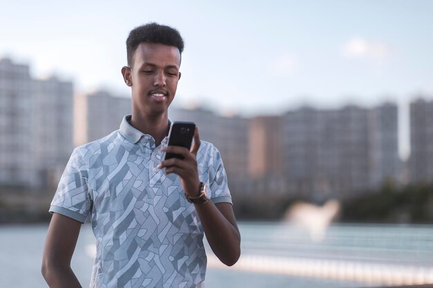 Junger schwarzer mann in lässiger kleidung, der eine sms mit seinem handykopienraum tippt, umfasst