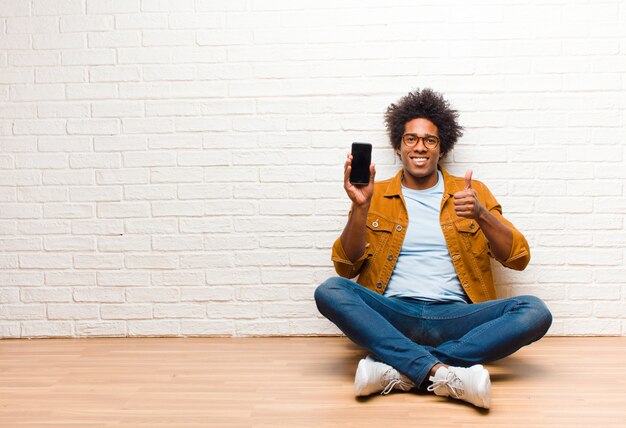 Junger schwarzer Mann mit einem Smartphone, das auf dem Boden sitzt