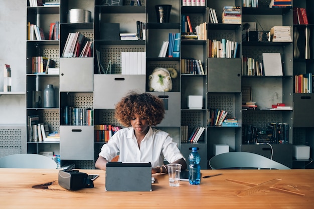 Junger schwarzer Student, der mit Tablette an einem Projekt in coworking Büro arbeitet