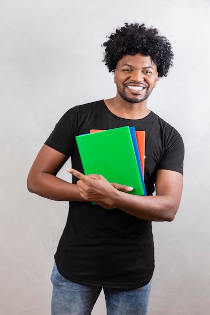 Junger schwarzer Studentenjunge mit Büchern und Notizbüchern im Hintergrund