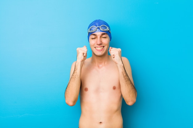 Junger Schwimmermann, der Faust anhebt, glücklich und erfolgreich sich fühlt. Sieg-Konzept.