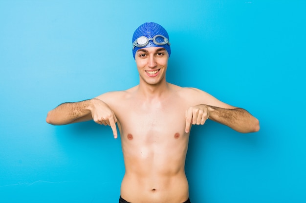 Junger Schwimmermann zeigt unten mit den Fingern, positives Gefühl.