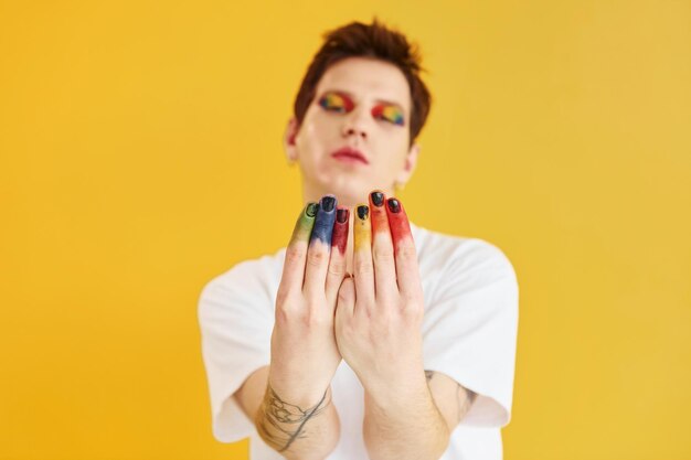 Junger schwuler Mann steht im Studio und posiert für eine Kamera Regenbogen-Make-up