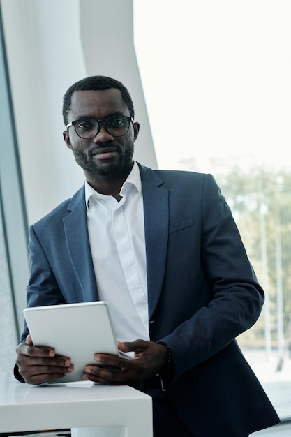 Junger selbstbewusster afrikanisch-amerikanischer Makler im Anzug mit Tablet im Büro