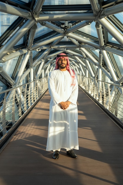 Junger selbstbewusster Geschäftsmann oder Delegierter in nationaler arabischer Kleidung, der auf einem langen Gang im Geschäftszentrum vor der Kamera steht