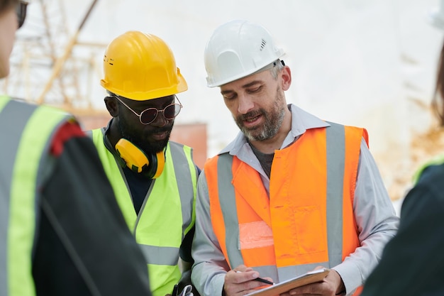 Junger selbstbewusster Vorarbeiter erklärt männlichen Untergebenen Punkte des Arbeitsplans