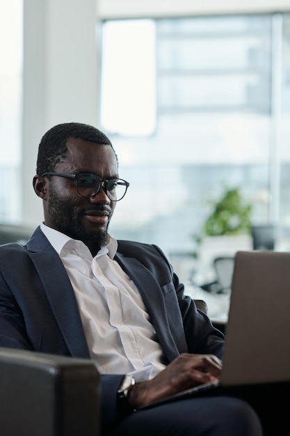 Junger seriöser Makler oder Analyst im eleganten Anzug, der auf den Bildschirm des Laptops blickt