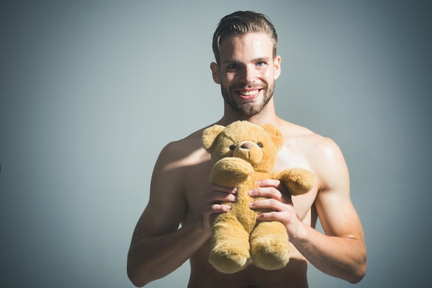 Junger sexy attraktiver Kerl mit hübschem Mann des Spielzeugbären mit seinem lächelnden bärtigen Mann des Teddybären, der hält