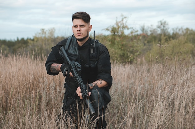 Junger Soldat in schwarzer Uniform sitzt mit einem Sturmgewehr