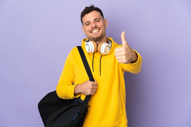 Junger Sportkaukasier mit Tasche, die mit Daumen oben isoliert wird, weil etwas Gutes passiert ist