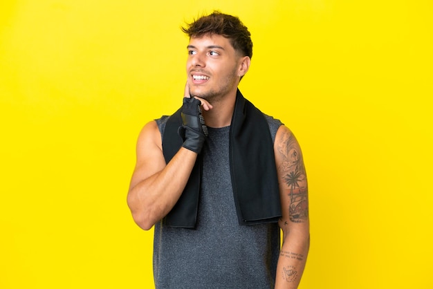Junger sportkaukasischer Mann mit Handtuch auf gelbem Hintergrund isoliert, der beim Nachschlagen eine Idee denkt
