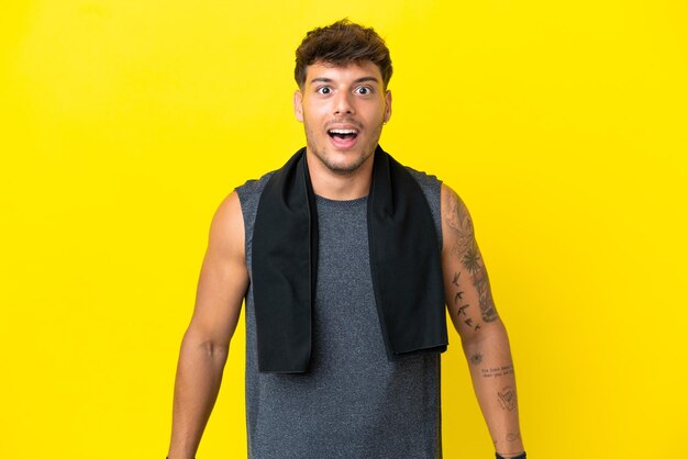 Junger sportkaukasischer Mann mit Handtuch auf gelbem Hintergrund mit Überraschungsgesichtsausdruck isoliert