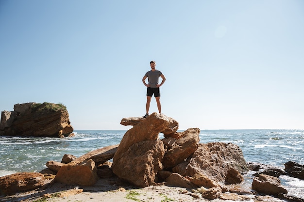 Junger Sportler, der an der Küste auf einem Felsen steht