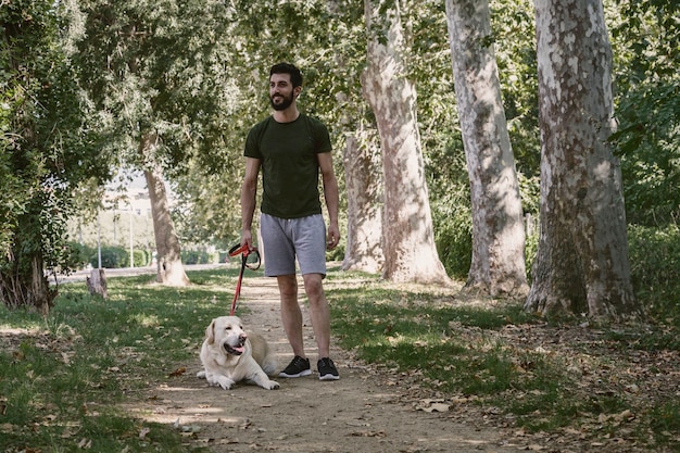 Junger Sportler, der an einem sonnigen Tag mit seinem kanadischen Labrador-Hund durch einen Stadtpark geht