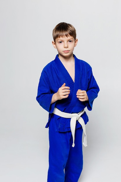 Junger Sportler im blauen Kimono für Sambo-Judo posiert auf weißem Hintergrund und sieht gerade aus