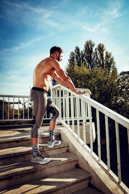 Junger Sportler ruht sich nach dem Training an der Brücke aus und schaut weg.