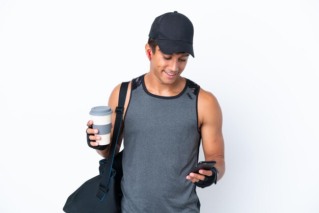 Junger sportlicher kaukasischer Mann mit Sporttasche isoliert auf weißem Hintergrund mit Kaffee zum Mitnehmen und einem Handy
