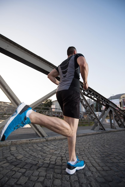 junger sportlicher Mann, der am sonnigen Morgen in der Stadt über die Brücke joggt